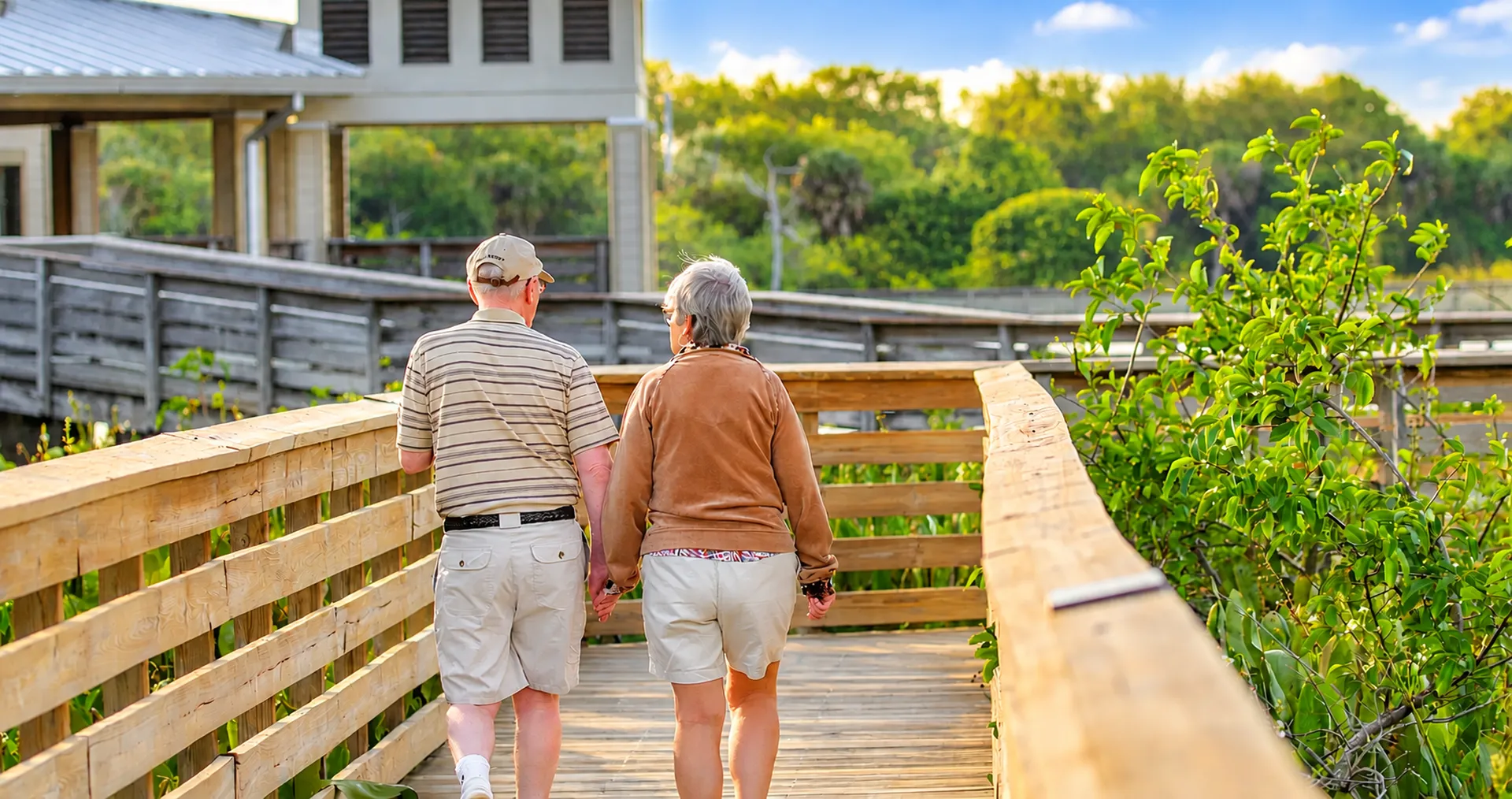 Two older people walking together along a garden boardwalk