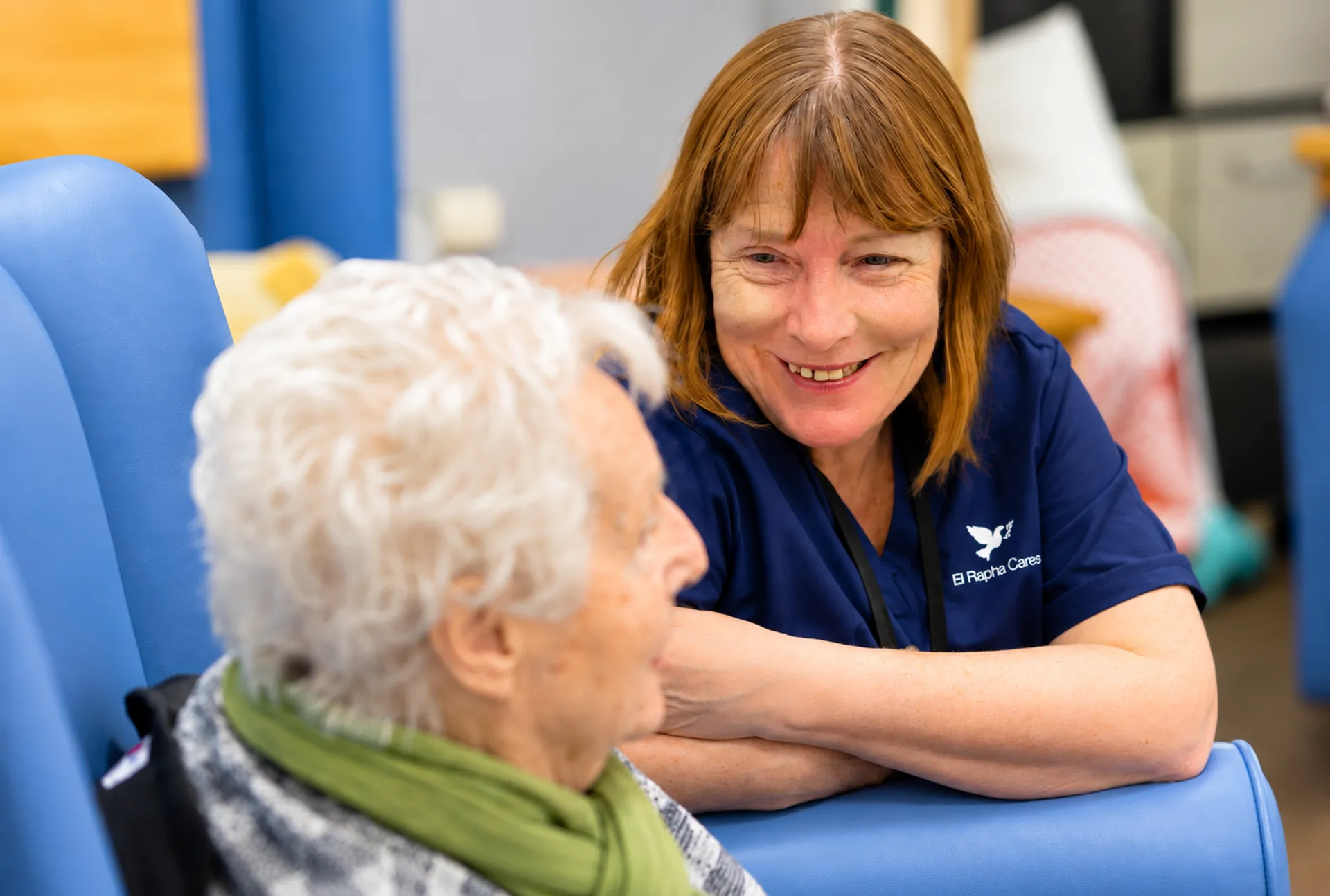 Carer chatting warmly with an elderly woman in an armchair