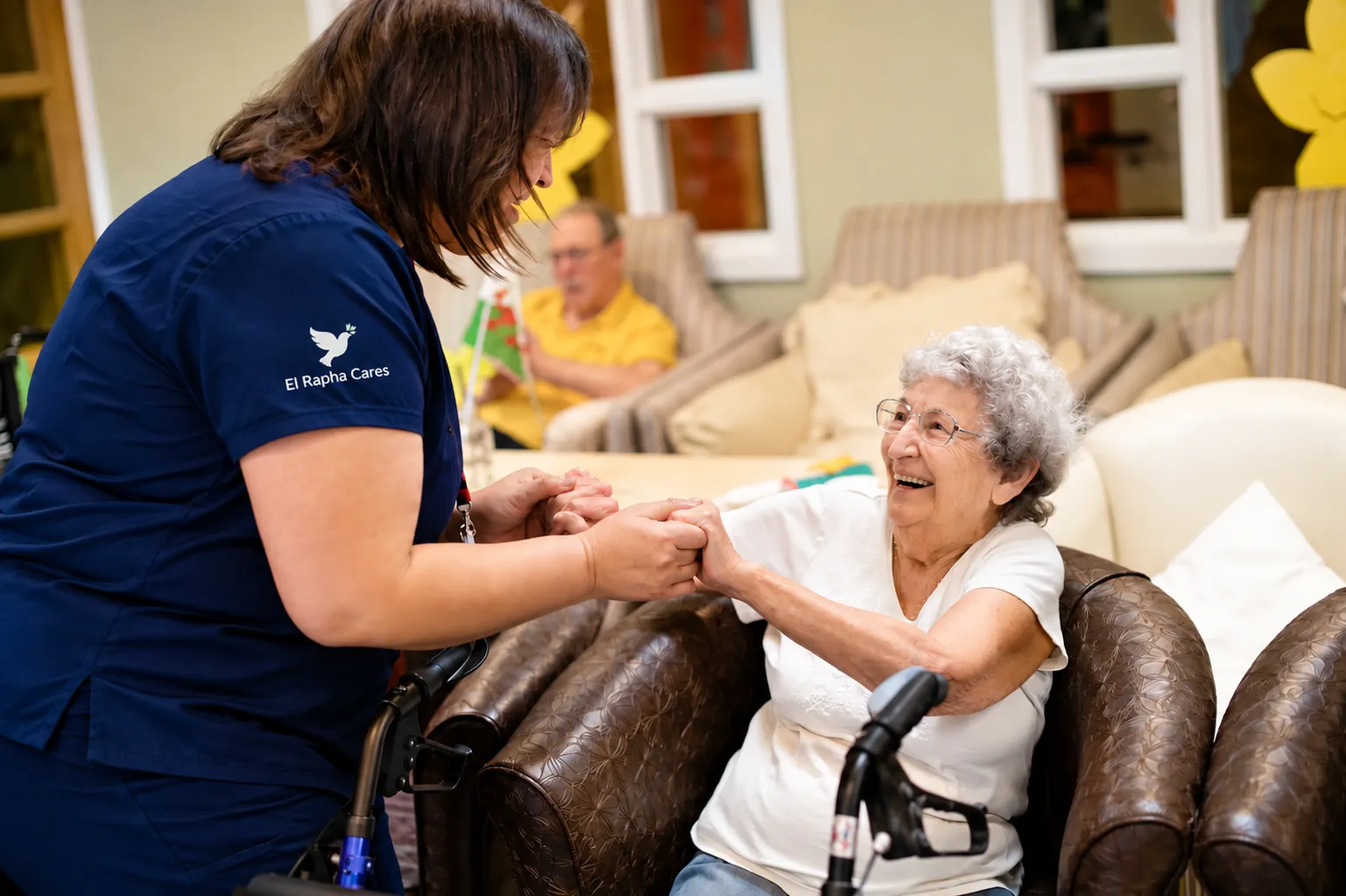 Carer holding hands with a smiling elderly woman in an armchair